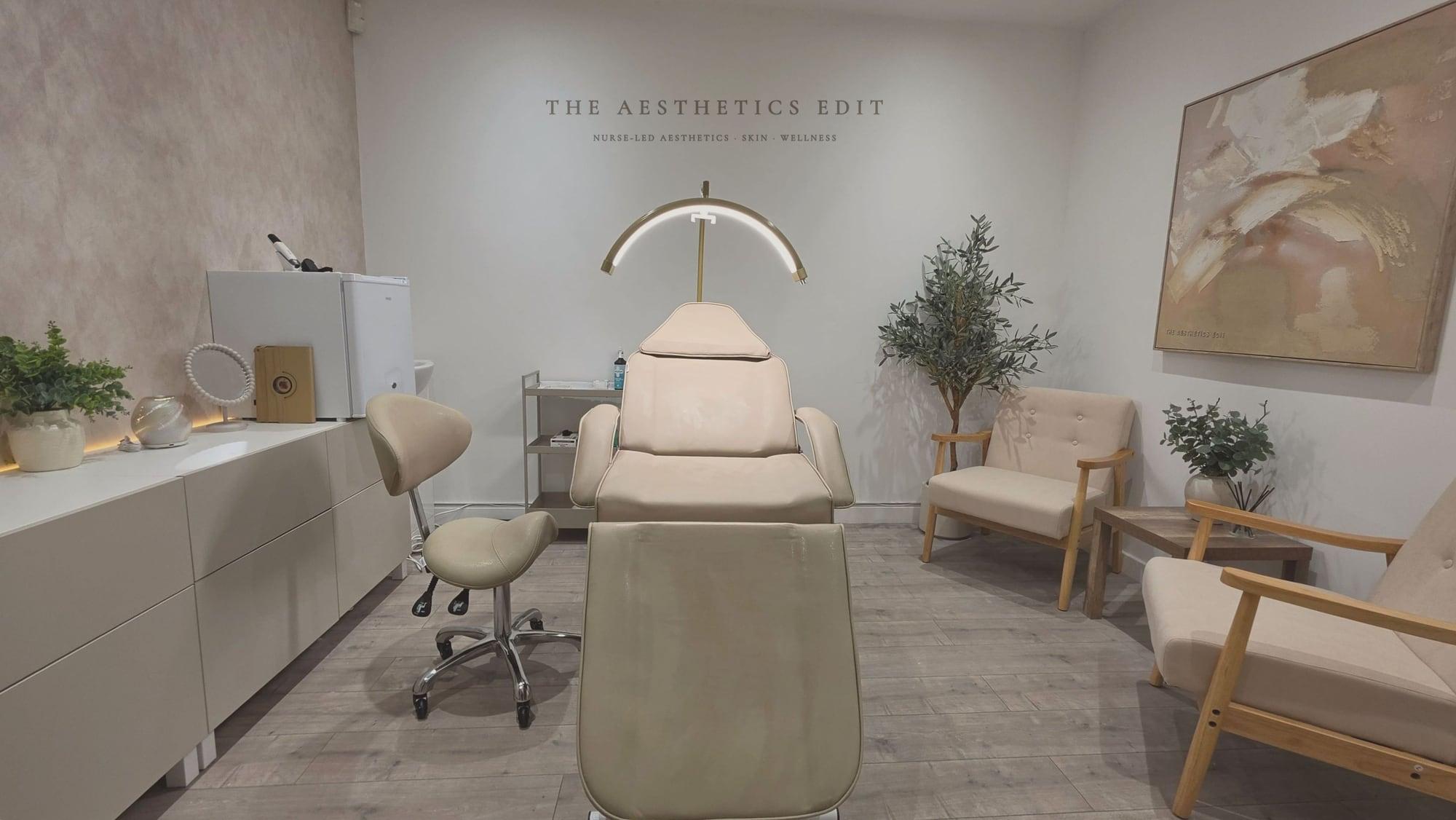 The treatment room at The Aesthetics Edit, with the clinic logo on the wall above a cream treatment chair