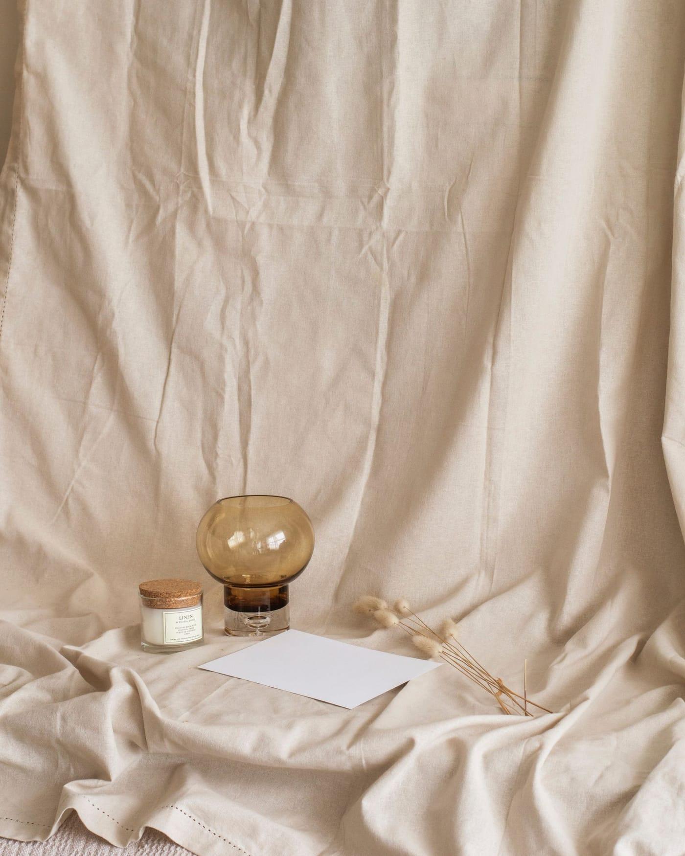 An amber glass vase and a card resting on draped cream linen