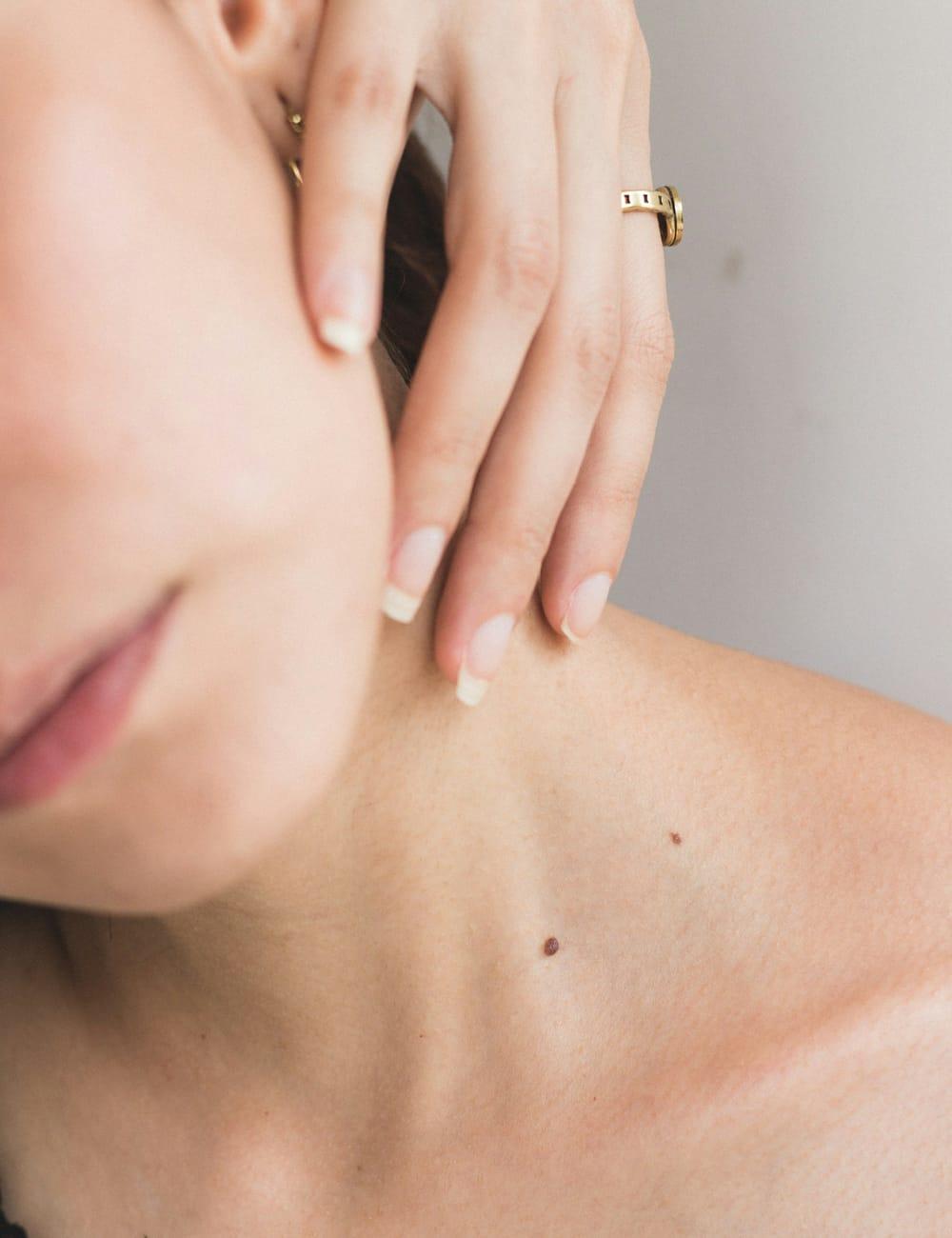Close-up of a woman's hand at her jaw and neck against a pale background