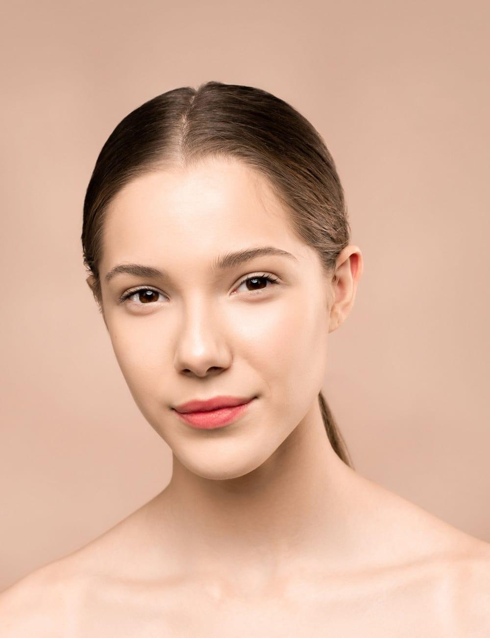 Portrait of a woman with smooth, radiant skin against a warm peach background