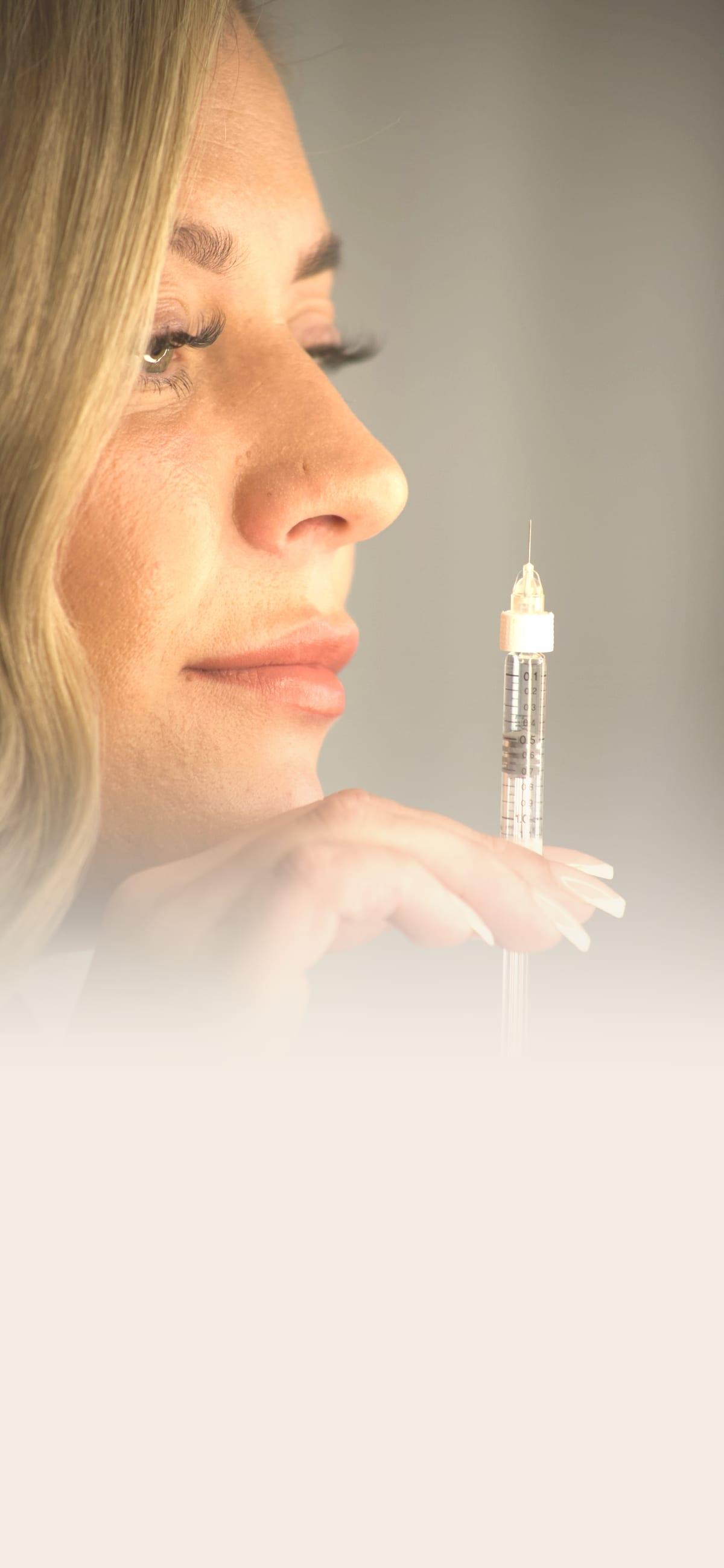 Chelsea Smith in profile, holding a filler syringe at her fingertips against a soft, warm backdrop
