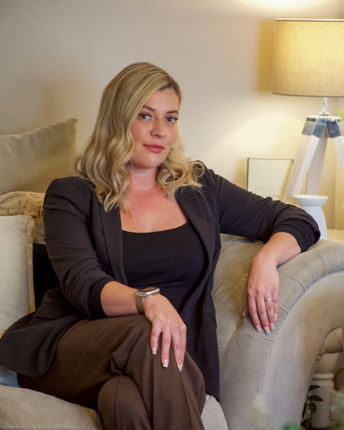 Chelsea Smith in a black blazer, seated on a linen sofa beside a softly lit lamp