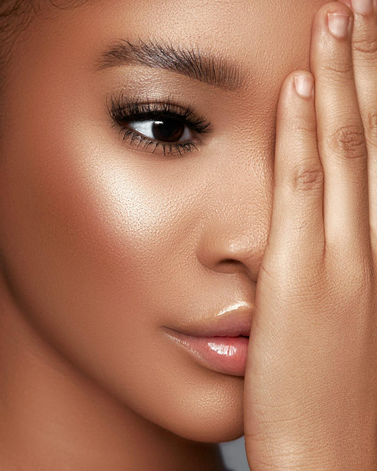 Close-up of a woman's glowing, dewy skin with one hand resting over her eye