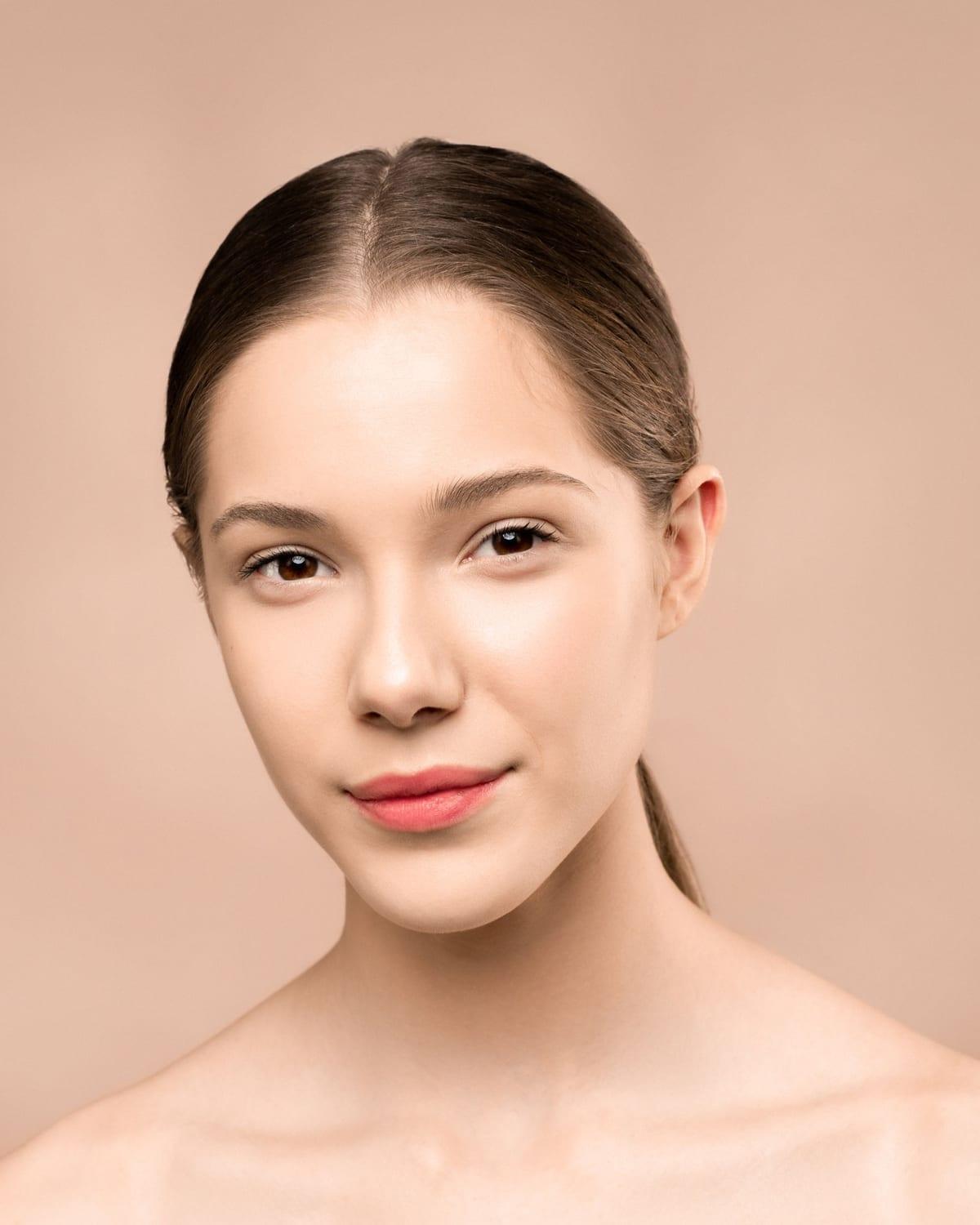 Portrait of a woman with smooth, radiant skin against a warm peach background