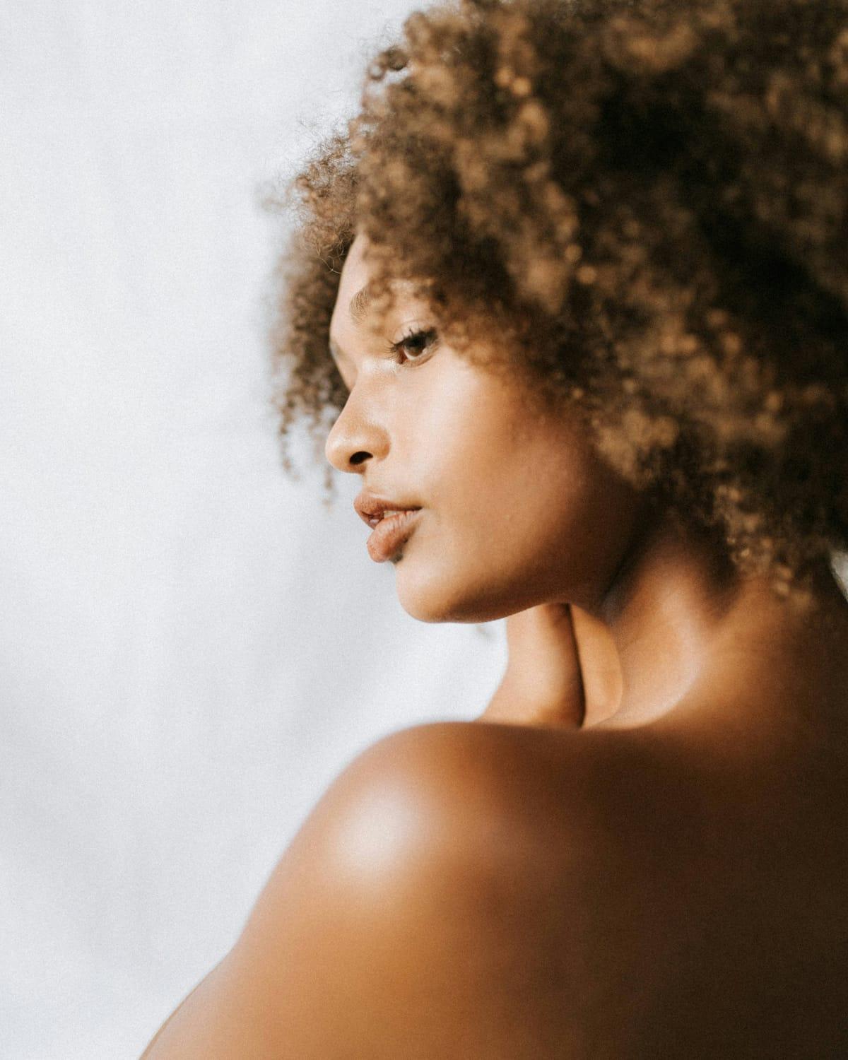 Side profile of a woman's jaw, neck and bare shoulder against a pale background