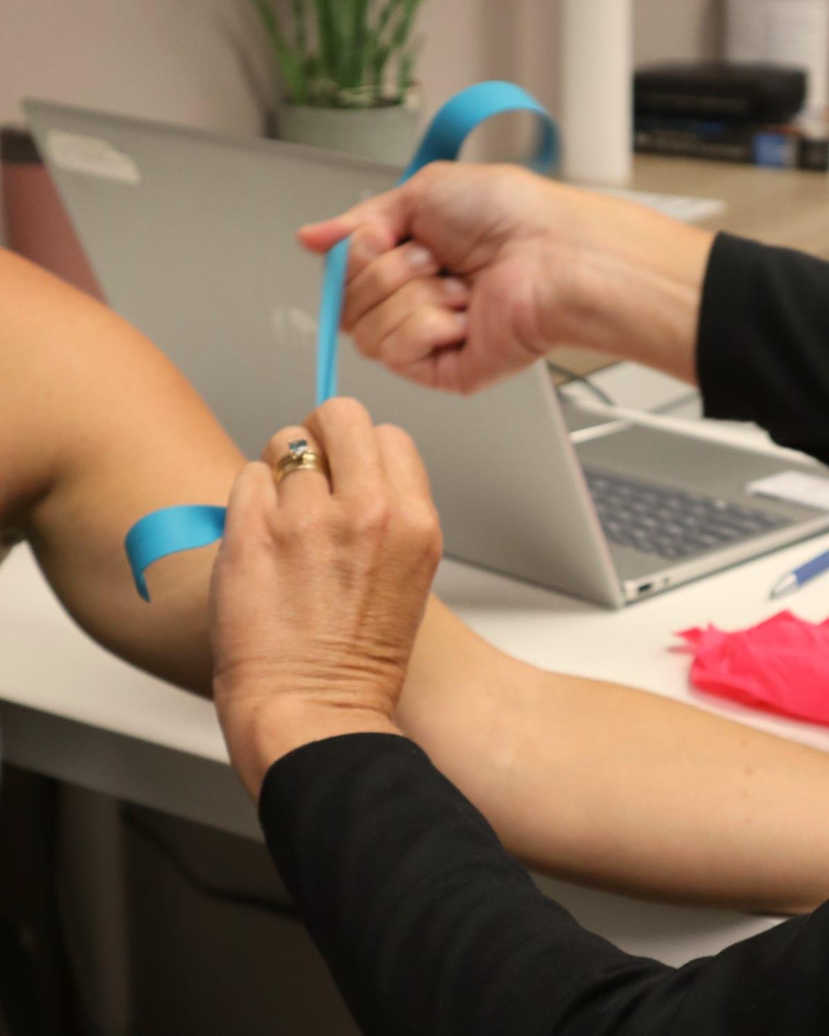 A practitioner tying a soft blue tourniquet around a client's upper arm before a blood draw